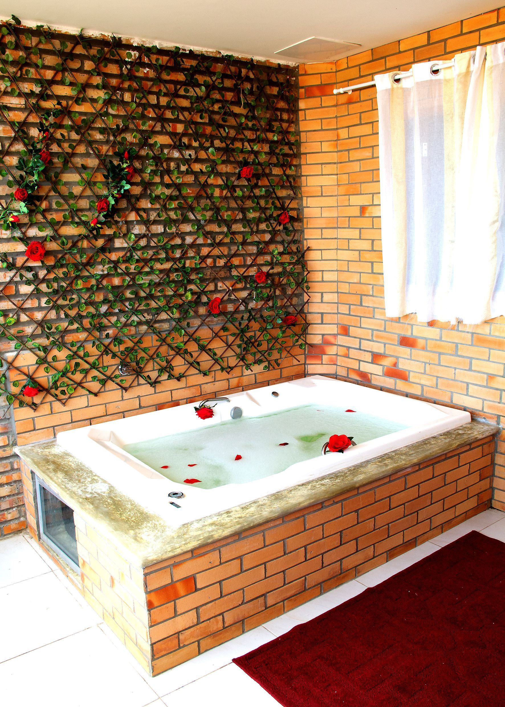 Uma casa de banho com banheira jacuzzi rodeada de tijolos e rosas.