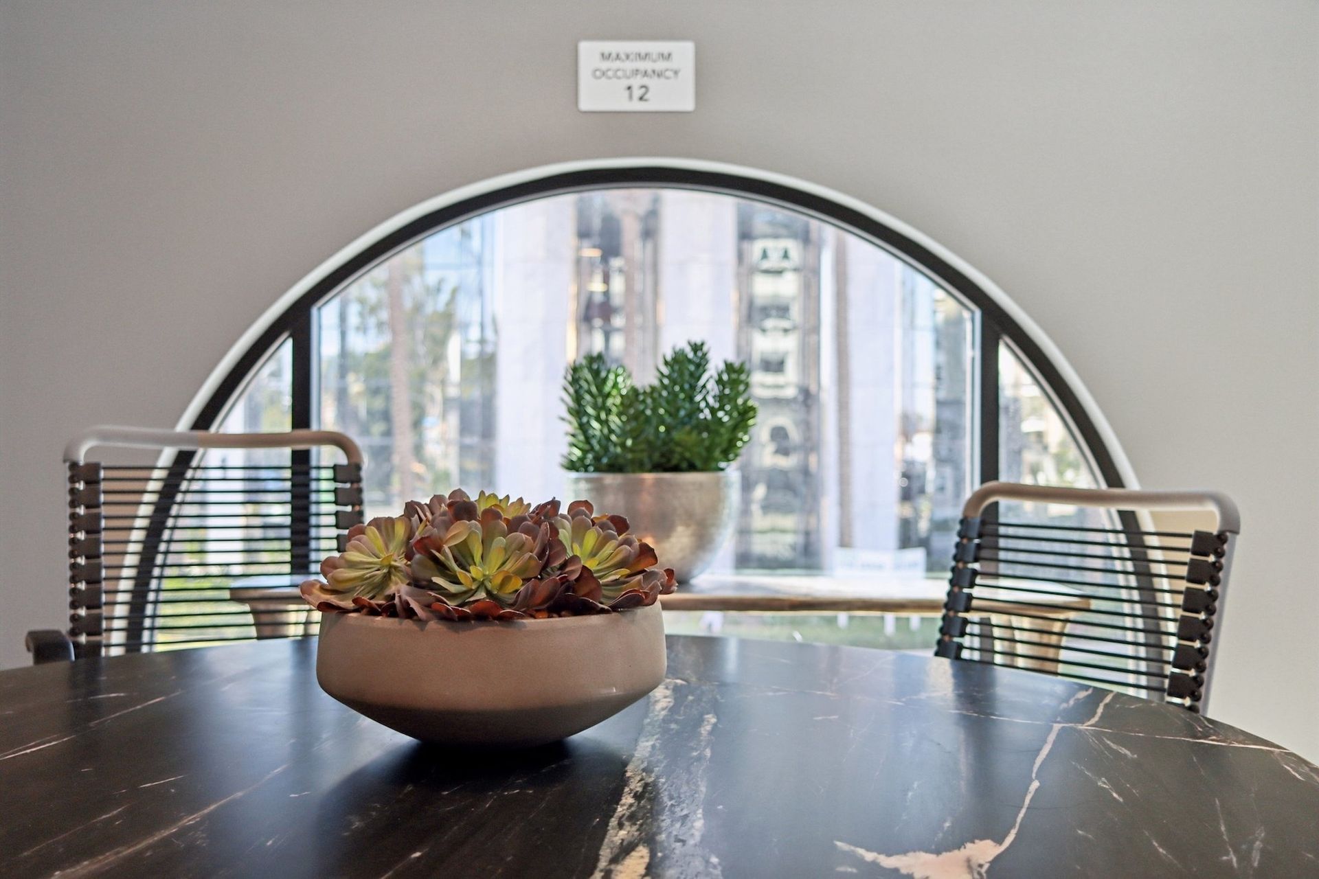 Round table with succulents in front of an arched window; two chairs and a cityscape view.