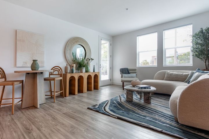 A bright, modern living room featuring a curved sofa, patterned rug, arched console table, and a small dining area.