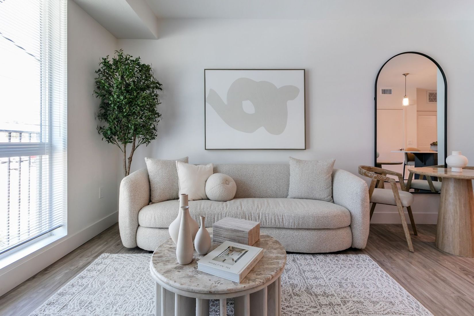 Bright living room with beige sofa, woven coffee table, large window, and a pink-lit dining nook
