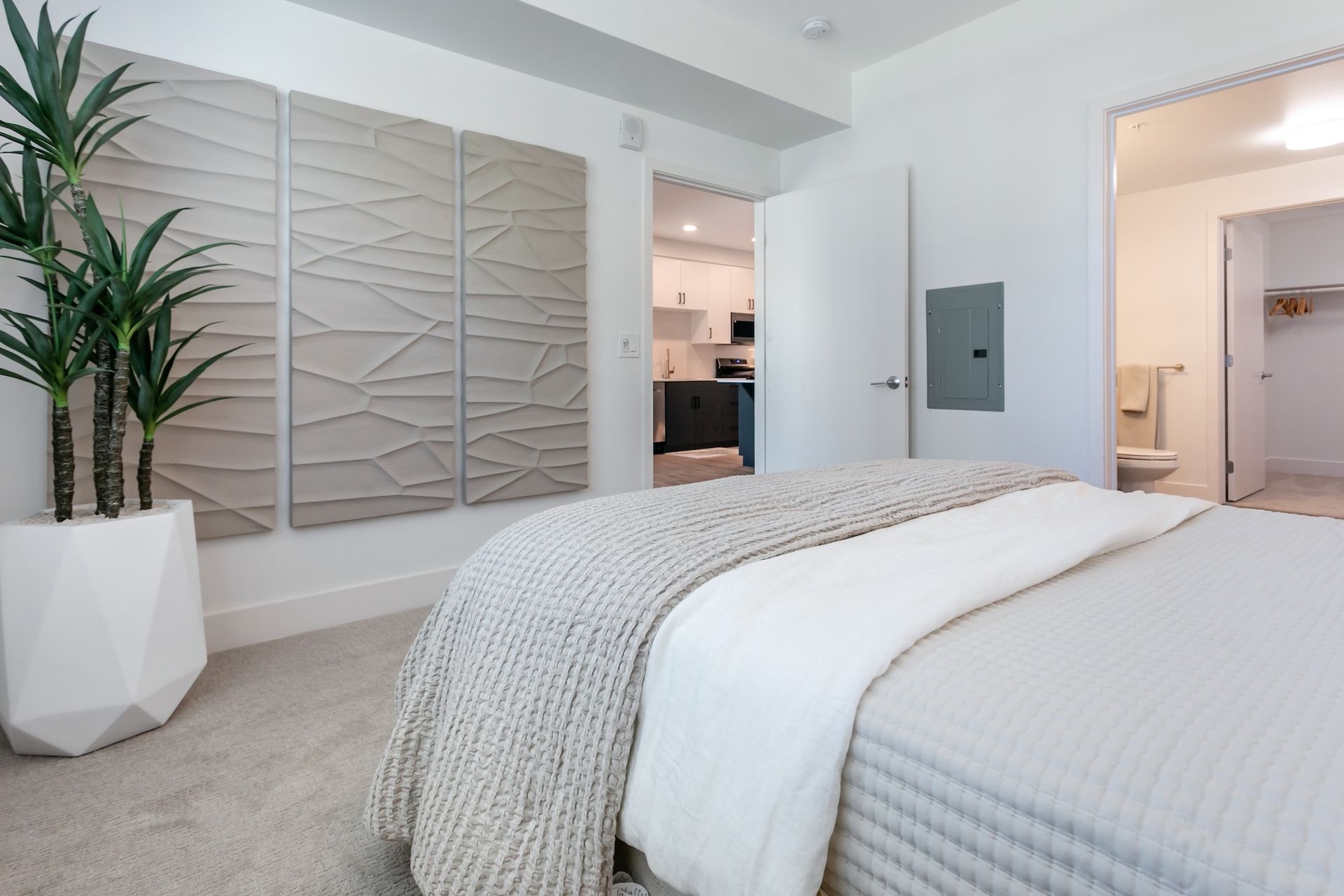 Bedroom with bed, plant, and decorative wall panels; door leads to kitchen and bathroom.