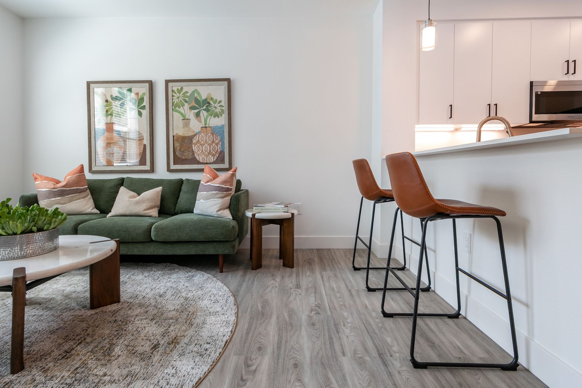 Living room with green sofa, bar stools, artwork, and marble coffee table.