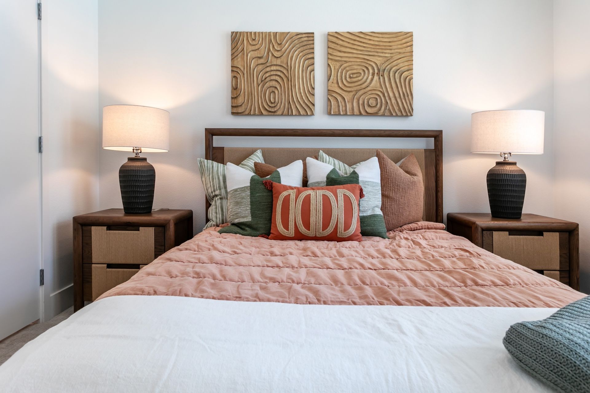 Bedroom with a bed, lamps, nightstands, decorative pillows, and wooden wall art.