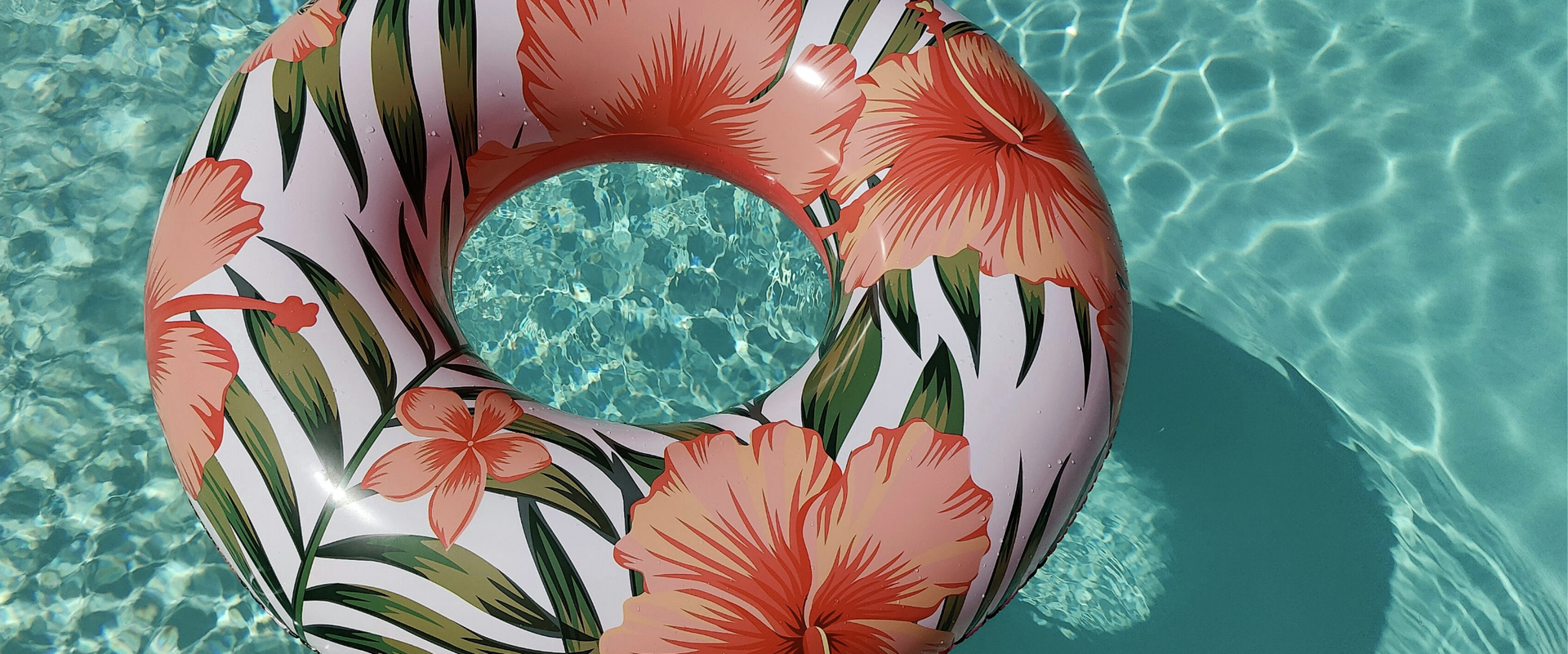 An inflatable ring with flowers and leaves is floating in a swimming pool.