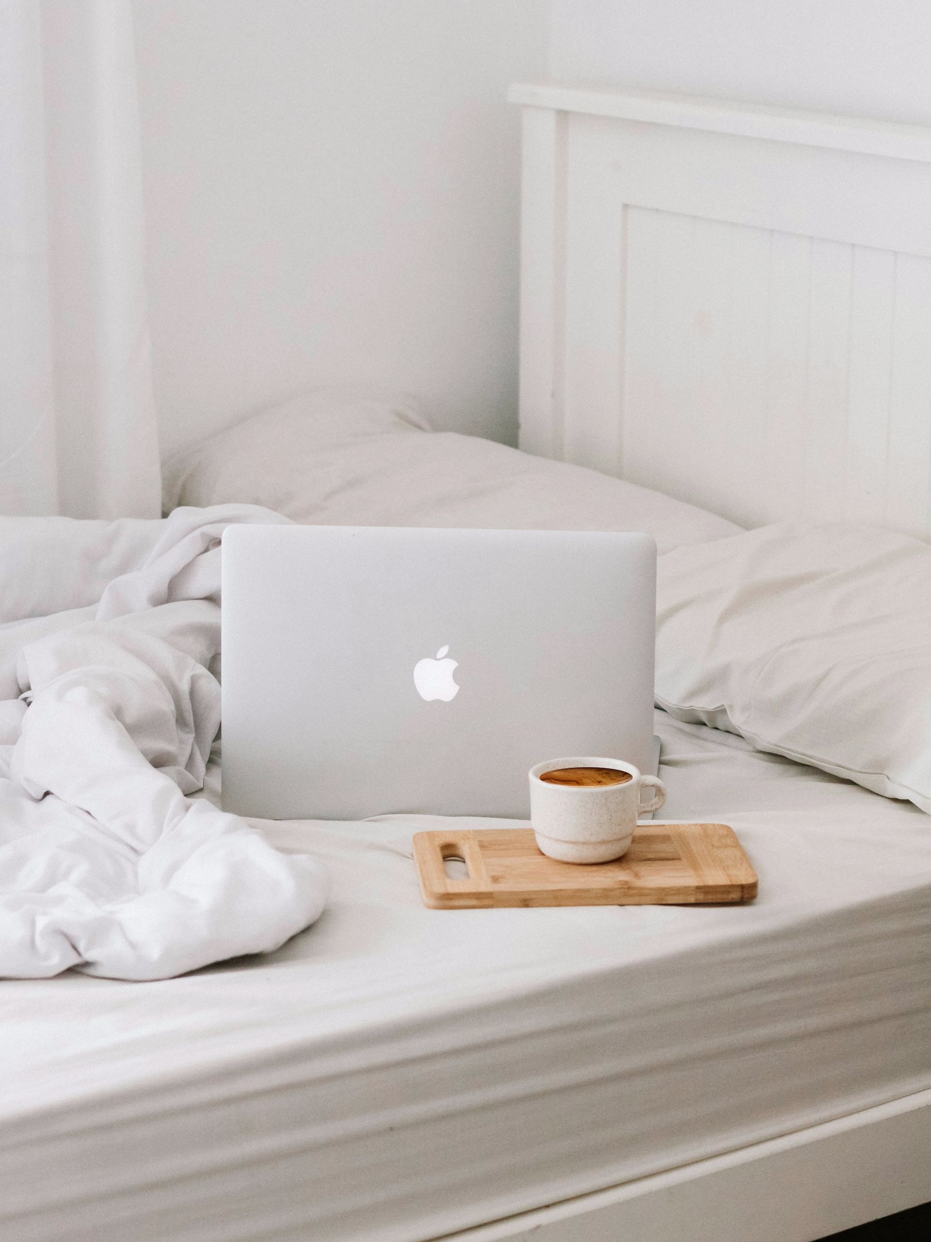 Laptop and coffee on a bed with white linens; wooden serving tray.