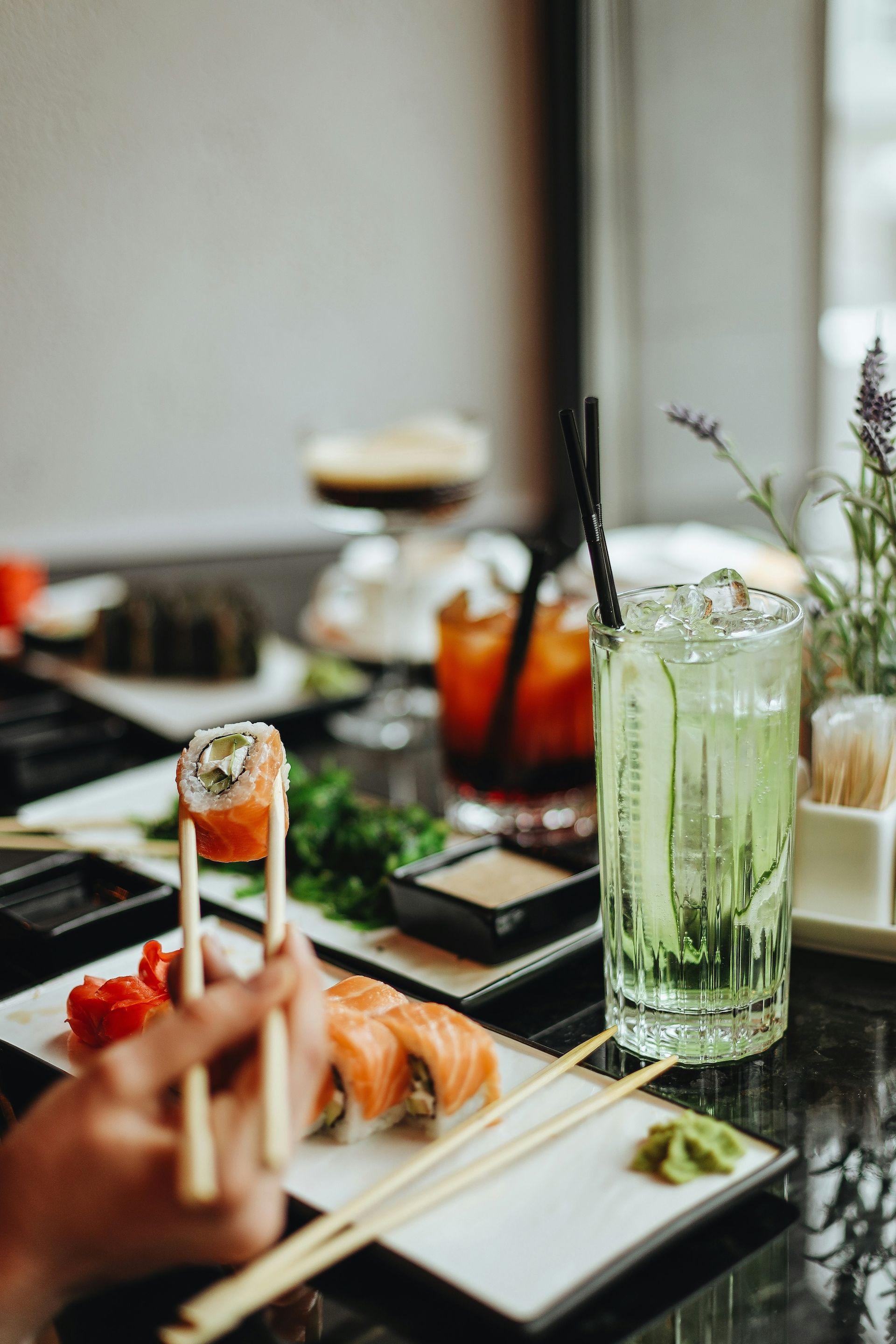 Person using chopsticks to eat sushi at a restaurant table with drinks.