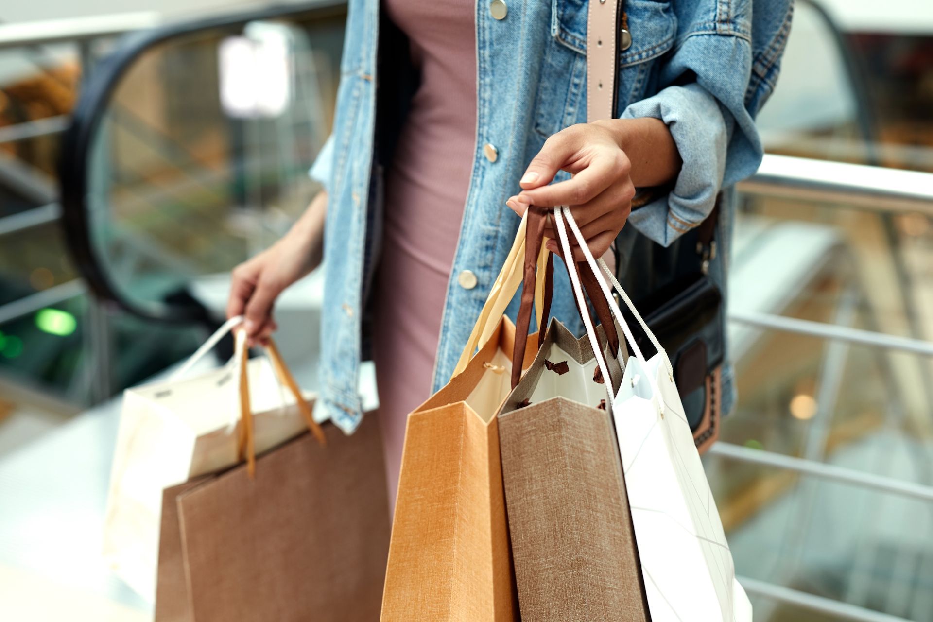 Person holding multiple shopping bags in a mall, next to an escalator.