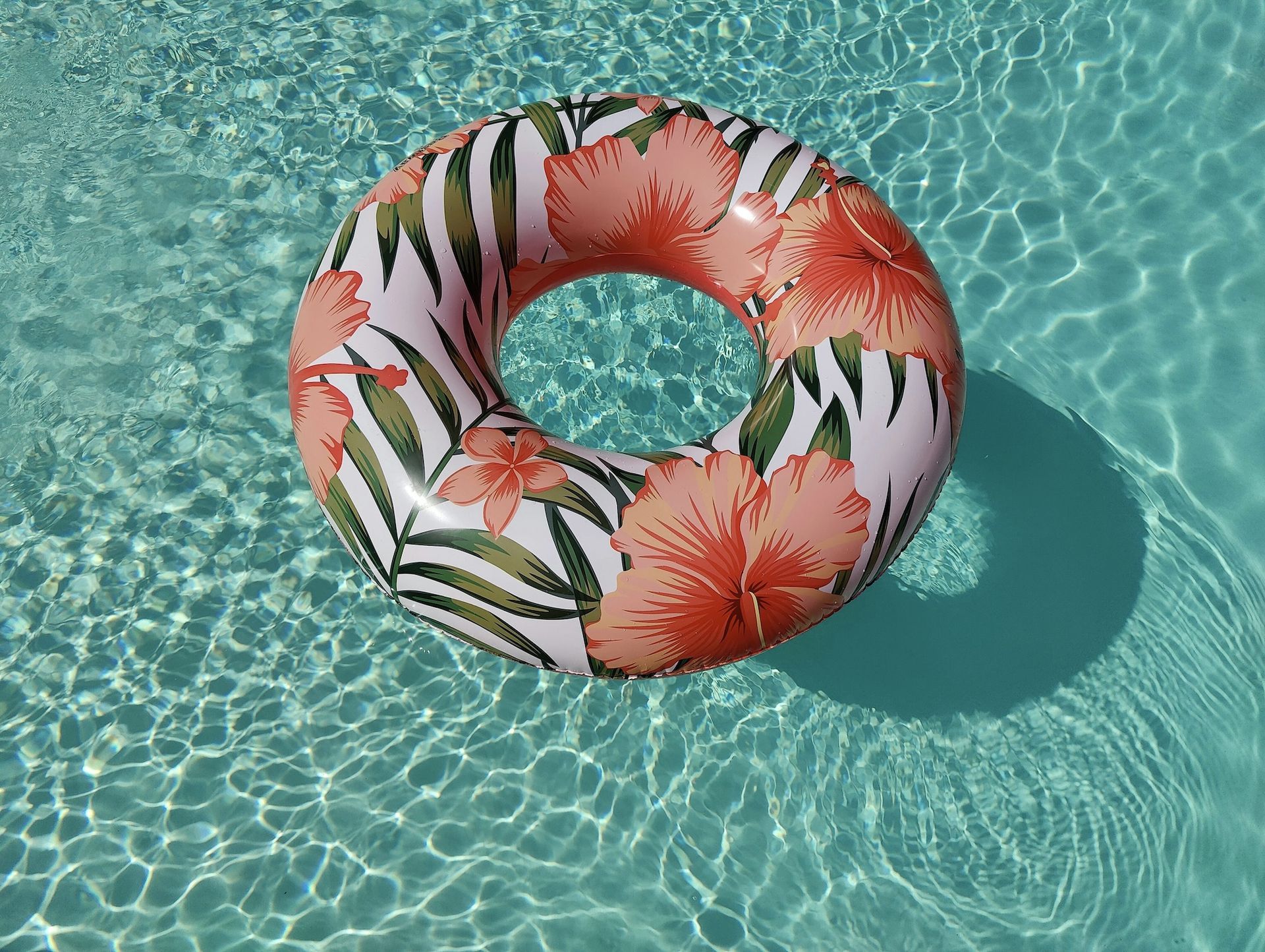 Inflatable pool ring with tropical floral design floating in clear blue water.