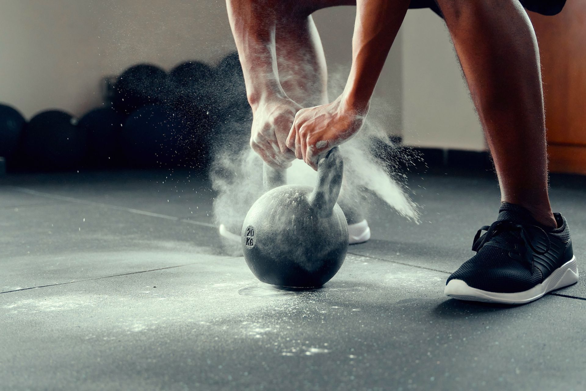 Person chalking hands over a kettlebell in a gym, preparing for a lift.