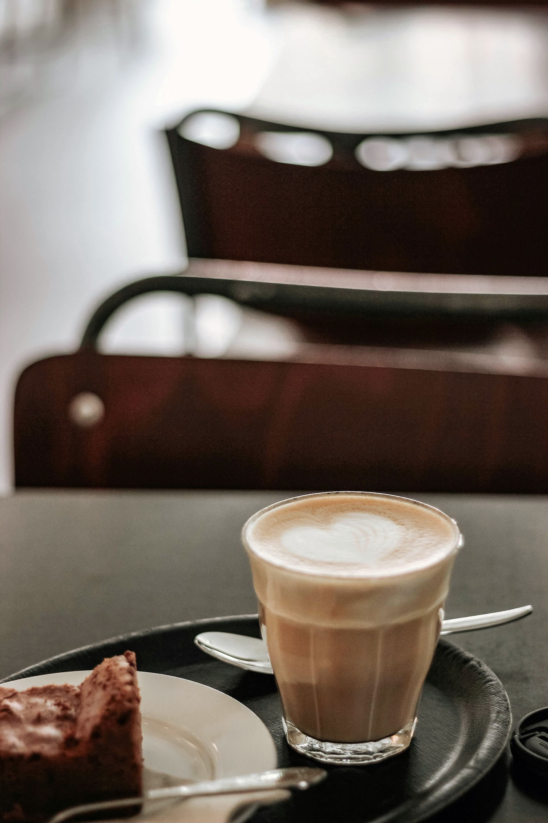 Latte in a glass, with foam, and a slice of cake on a plate, on a table.