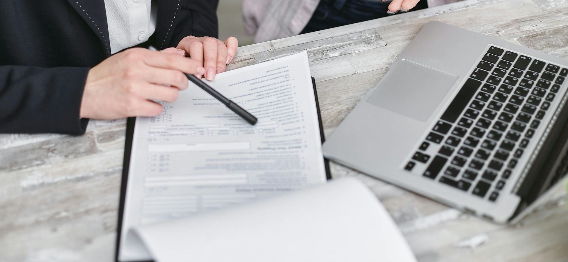 A person is sitting at a table with a laptop and a clipboard.