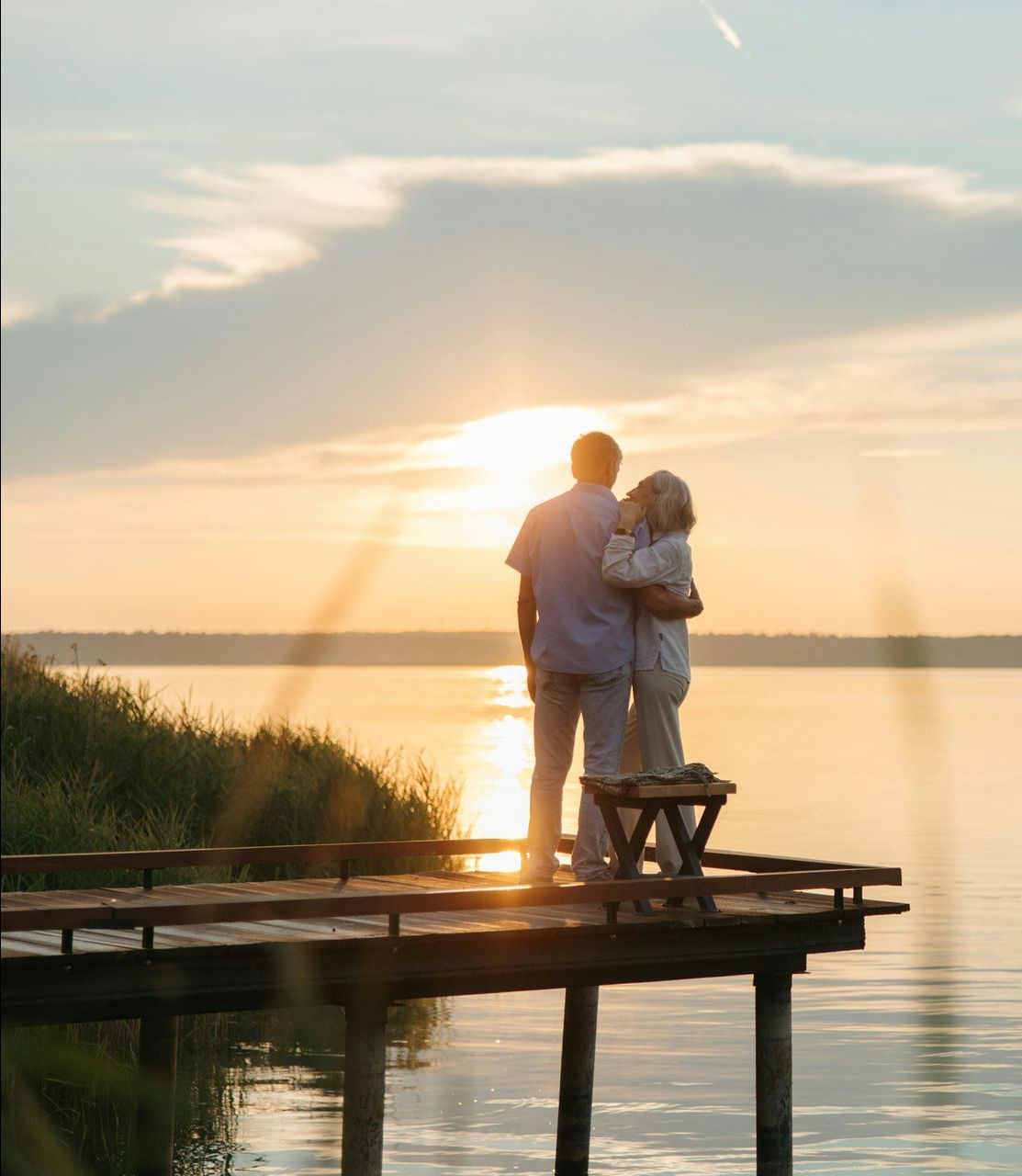 Couple hugging on a wooden pier, watching the sunset over a calm lake.