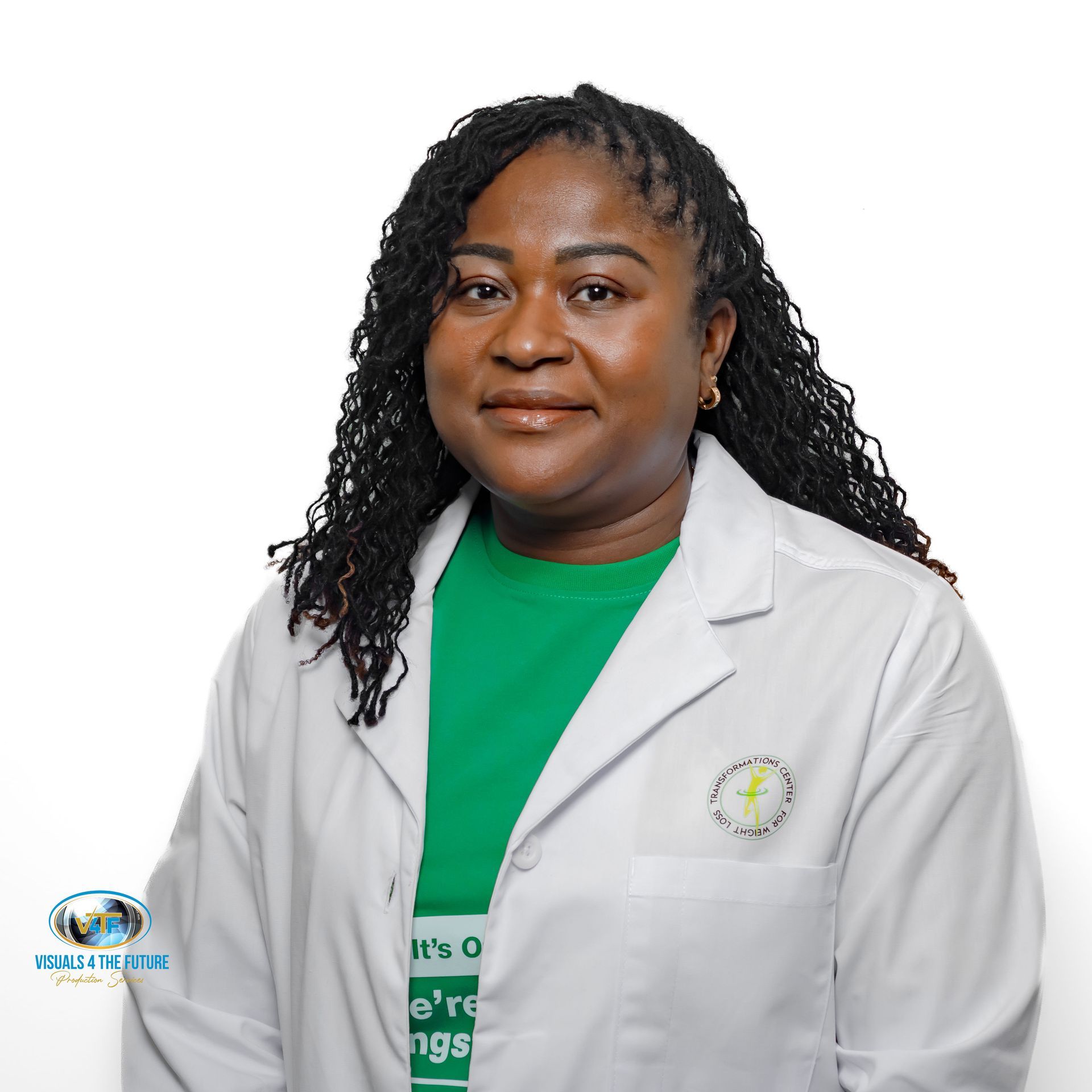 Woman in white lab coat with green shirt, wearing locs, smiling, studio shot.