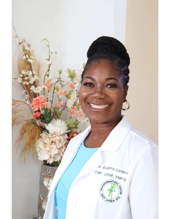 Woman in white lab coat smiles; seated, green background.