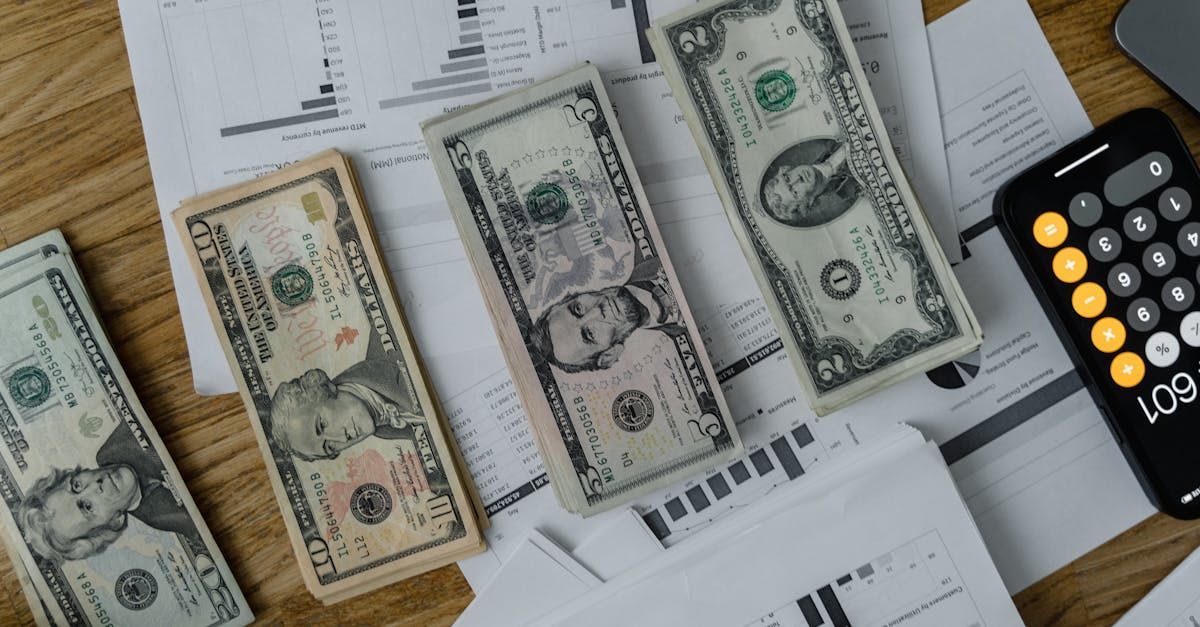 A bunch of money is sitting on top of a wooden table next to a calculator.