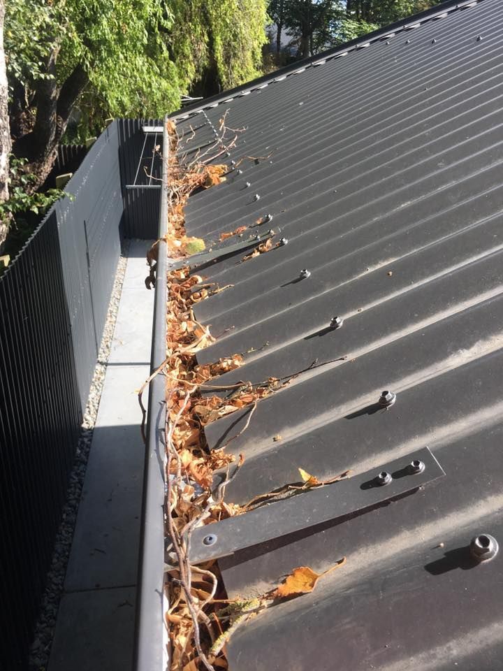 A black metal roof gutter filled with dead leaves and debris next to a dark wall.