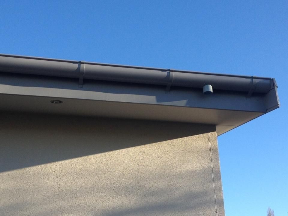 Gray rain gutter on a beige building corner against a clear blue sky.