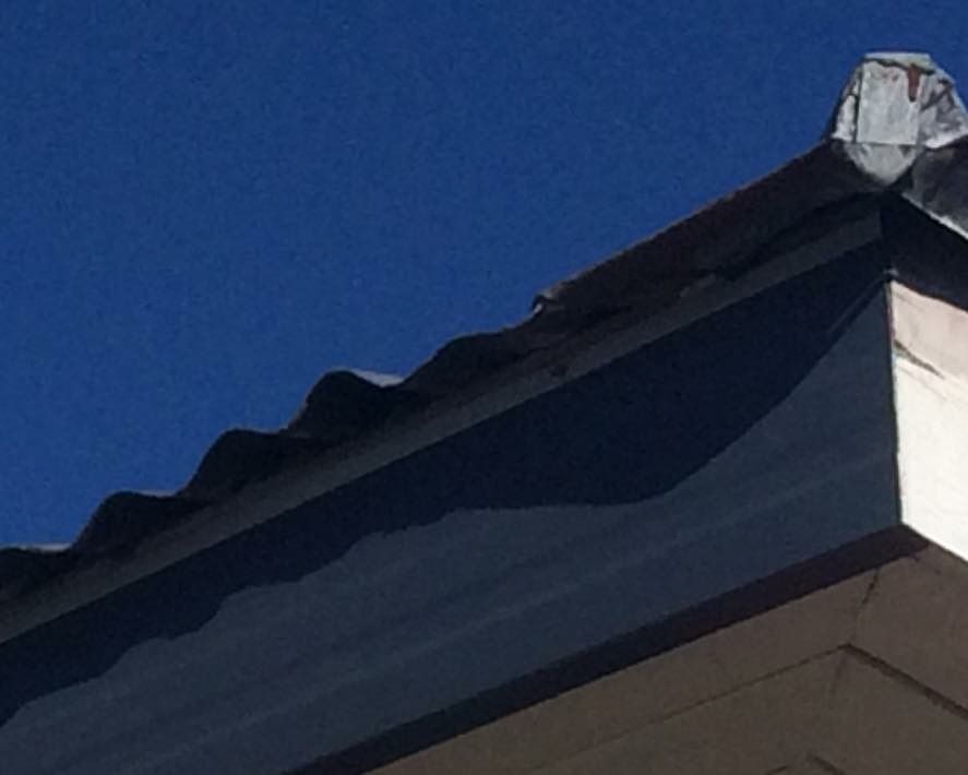Corner of a building with a corrugated metal roof against a clear blue sky. The roofline is partially visible.