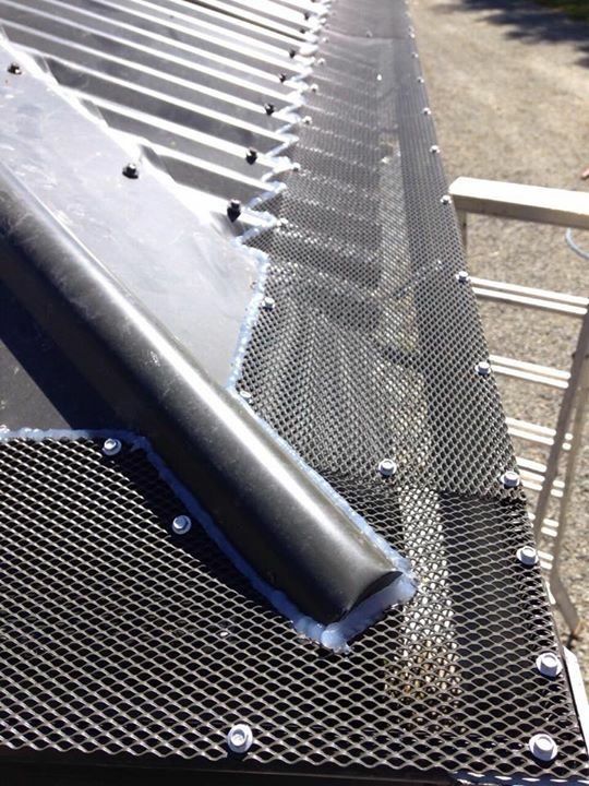 A close-up view of a gray corrugated metal roof with black gutter guards and a downspout secured with bolts.