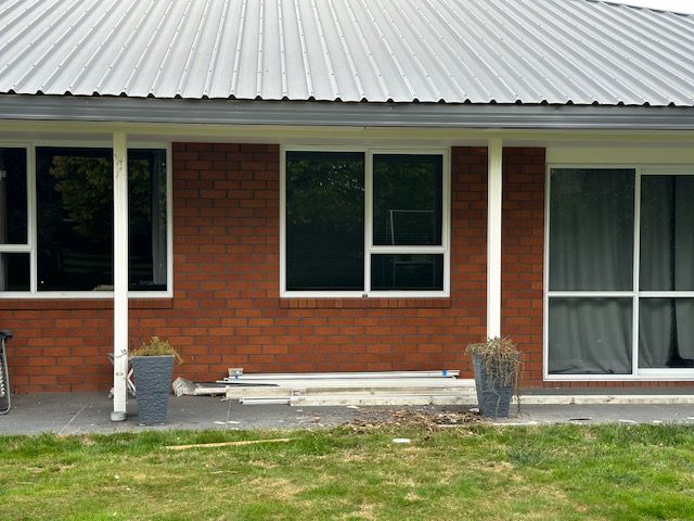 Red brick house exterior with a metal roof and multiple white-framed windows.  Green grass and gray pots sit below.