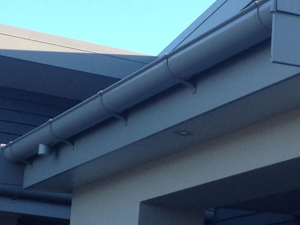 Gray gutters attached to a gray roof and a light tan wall.
