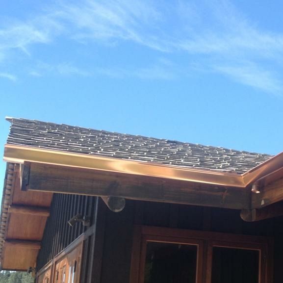Two gray garage doors between red brick pillars under a gray metal roof, greenery to the right, overcast sky.