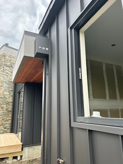 Dark gray metal siding on a modern building with a window and wooden entry.