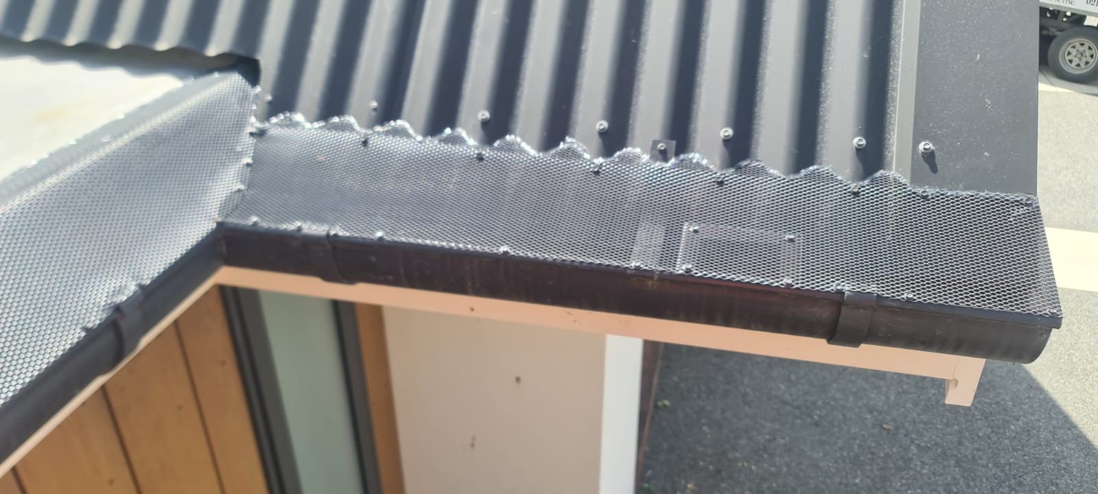 Close-up of a house roof with dark corrugated metal and installed gutter guards. The guards are dark mesh and sitting above the gutters.