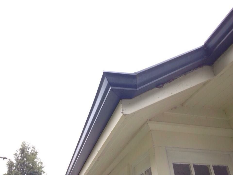 Dark gutters on a light-colored house. Angled shot of a corner, with a cloudy sky background.