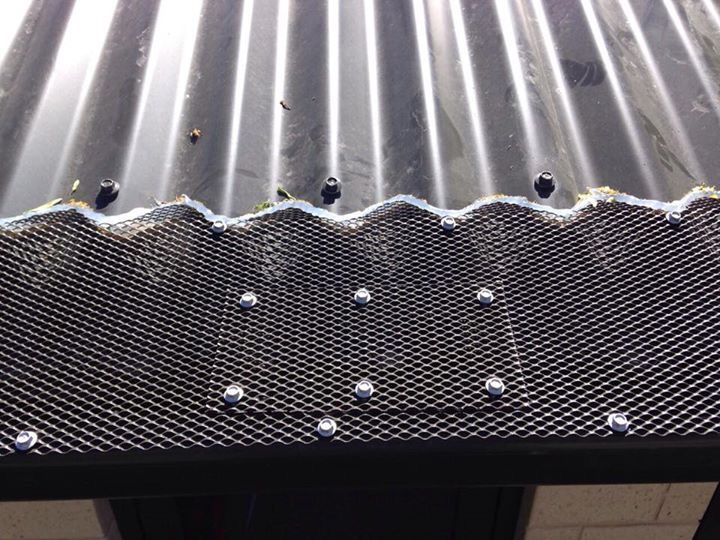 Close-up of black corrugated metal roof edge with attached black wire mesh, held in place by silver rivets.