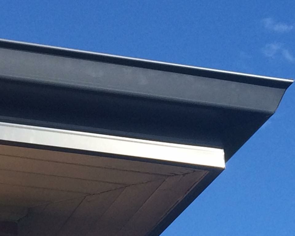 Dark gray rain gutter on a building's edge, against a bright blue sky.