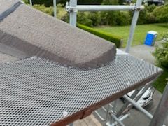 Metal gutter guard along the edge of a roof, with a concrete tile visible. Scaffolding and a blue portable toilet are in the background.
