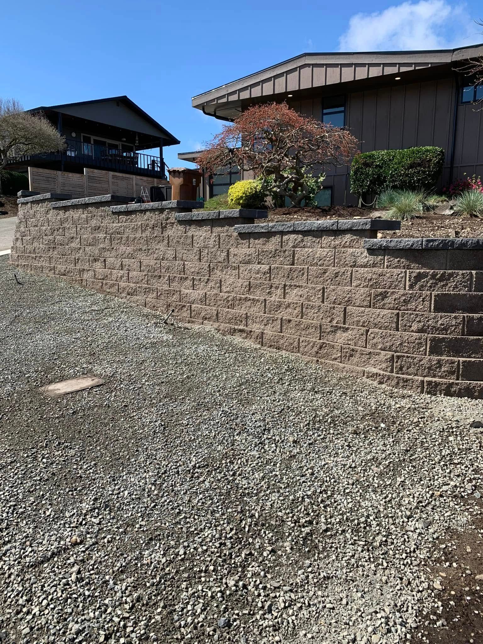 Stone retaining wall in front of a house with gravel and plants.