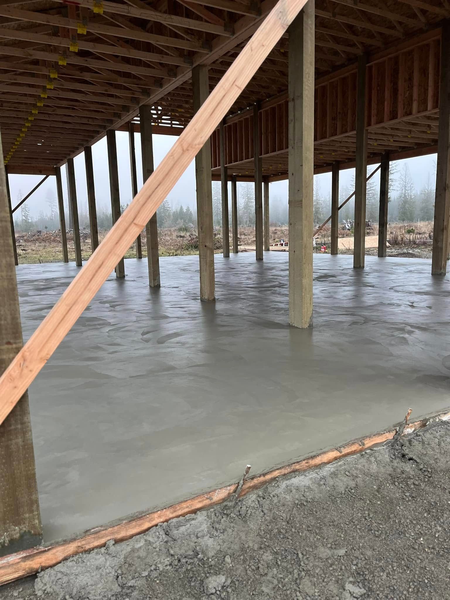 Newly poured concrete floor under a building under construction, supported by wooden posts.