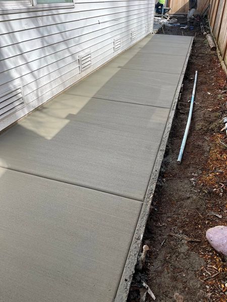 Newly poured concrete sidewalk next to a white building.
