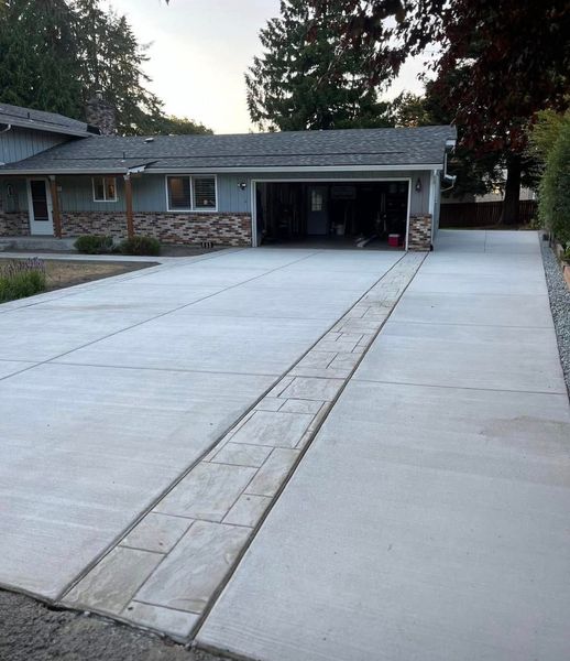 Concrete driveway leads to a garage; a decorative stone-like strip runs down the center.