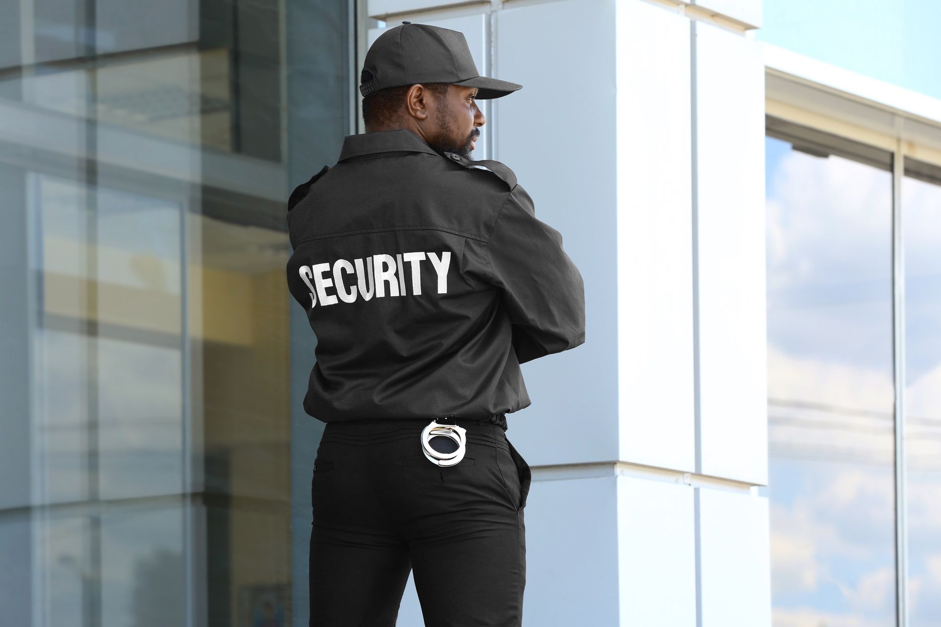 Security guard in black uniform standing outside a glass building, looking away.