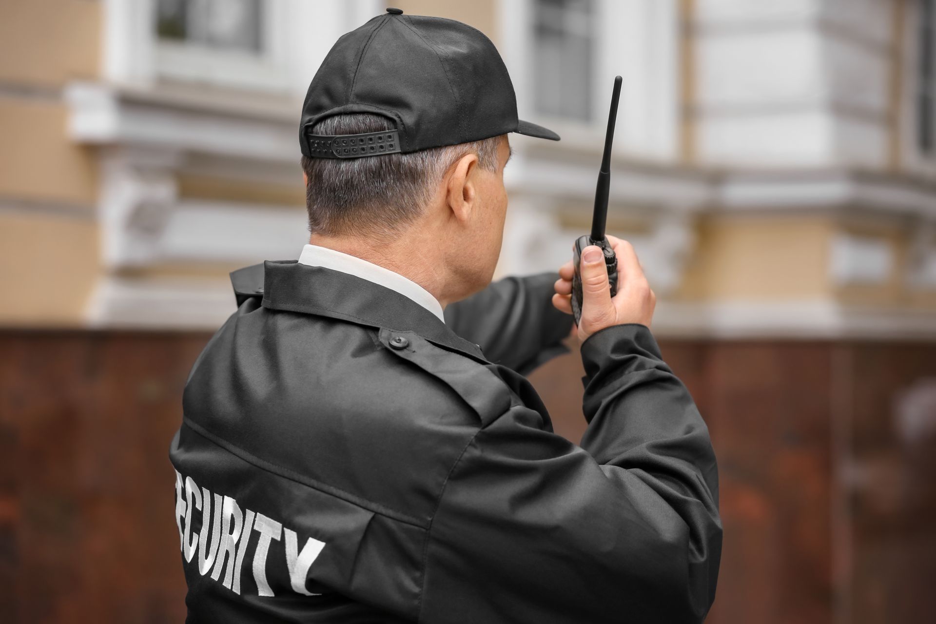 Security guard in black jacket using a walkie-talkie outdoors.