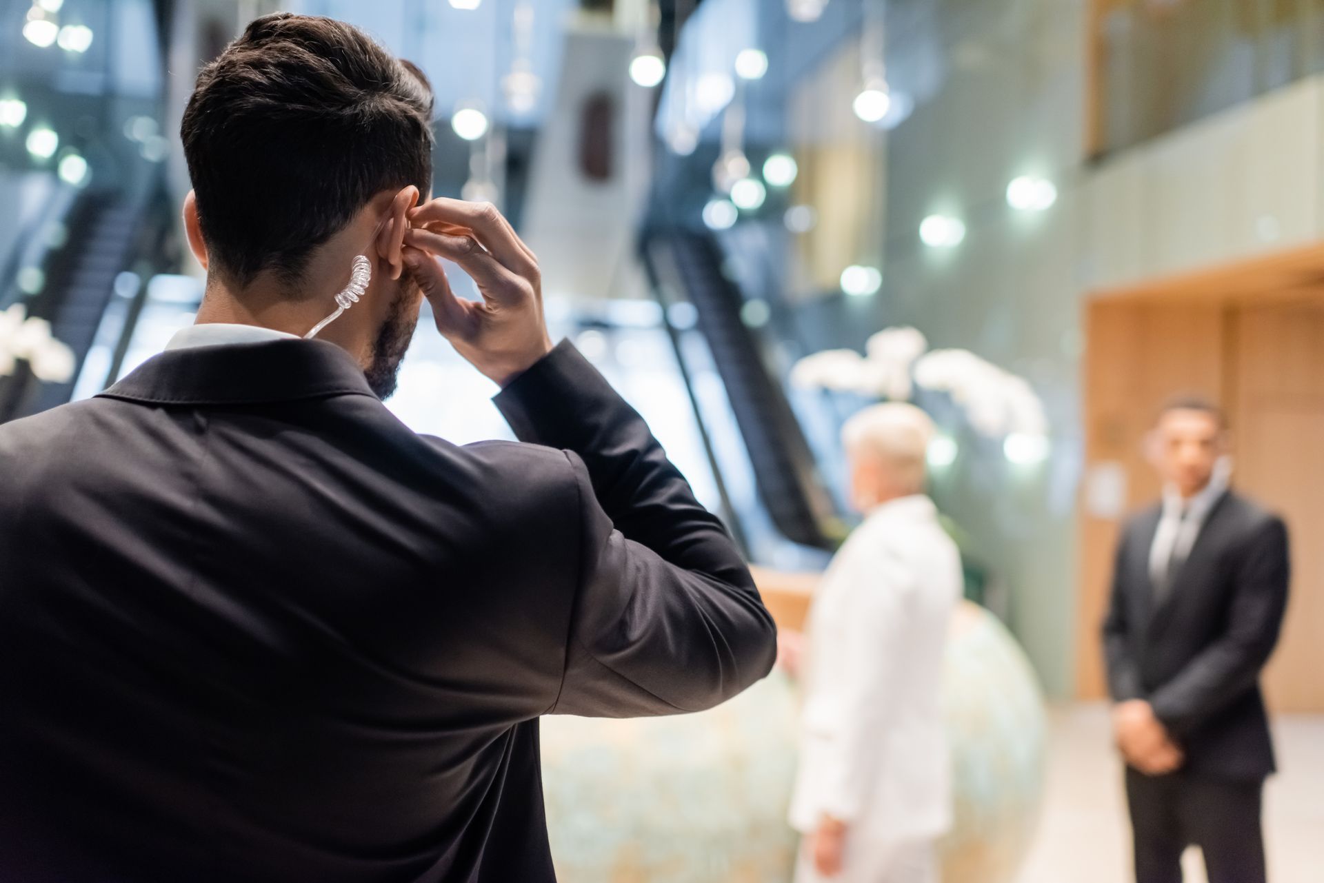 Man in a dark suit adjusting his earpiece while facing a formal event.