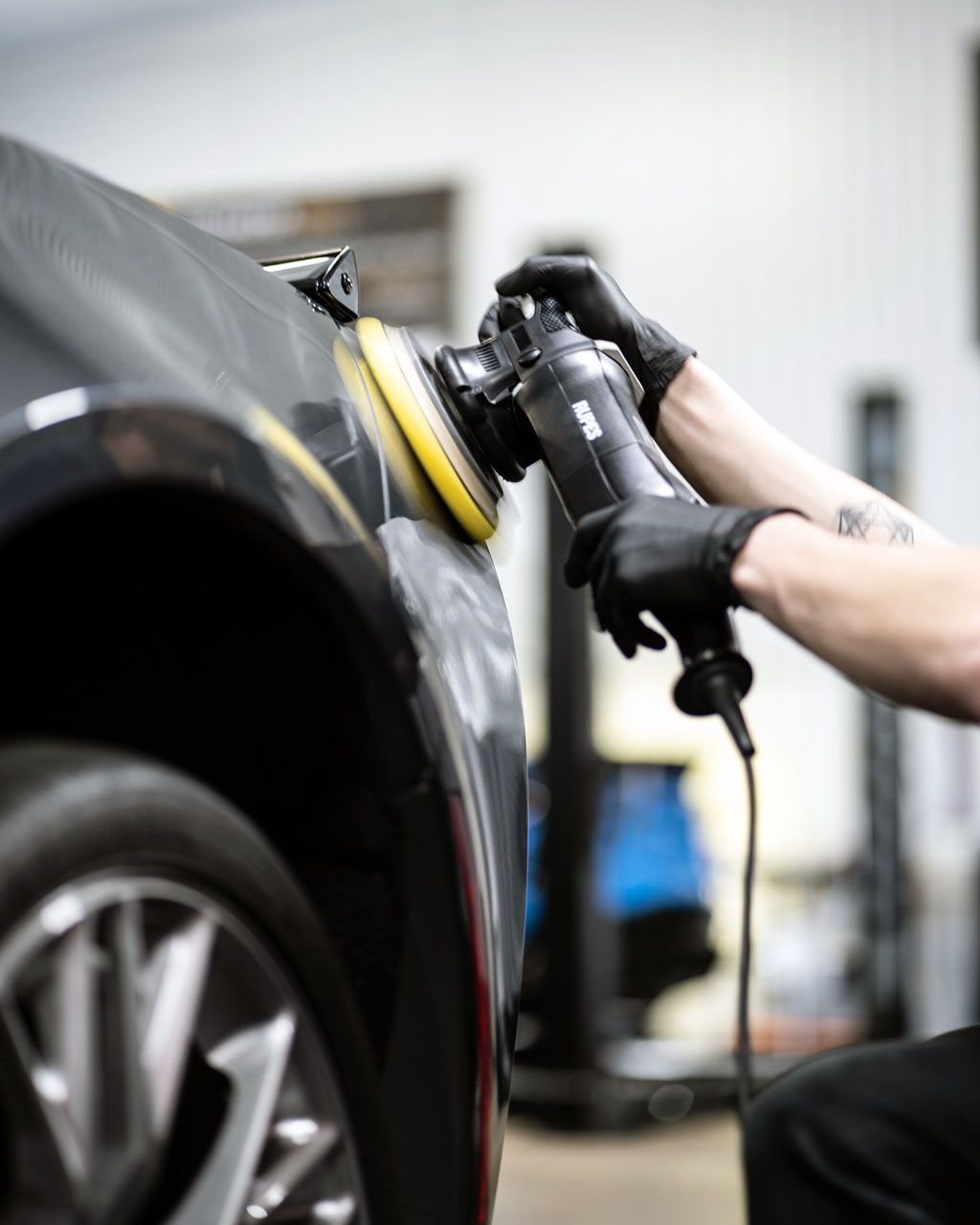 Technician polishing a black car with a buffer in an auto shop