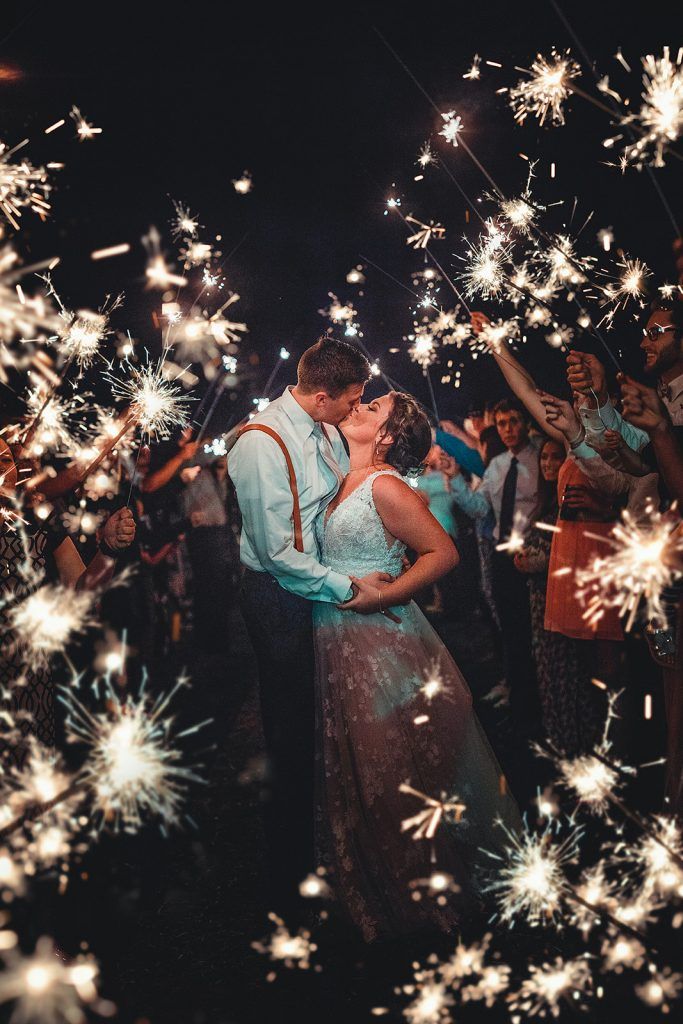 Couple kissing surrounded by sparklers at a wedding celebration, at night.