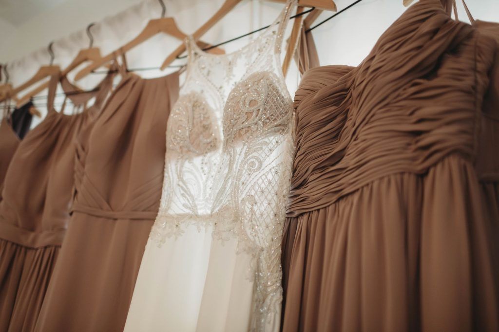 A row of brown bridesmaid dresses and a white lace wedding dress hanging on wooden hangers.