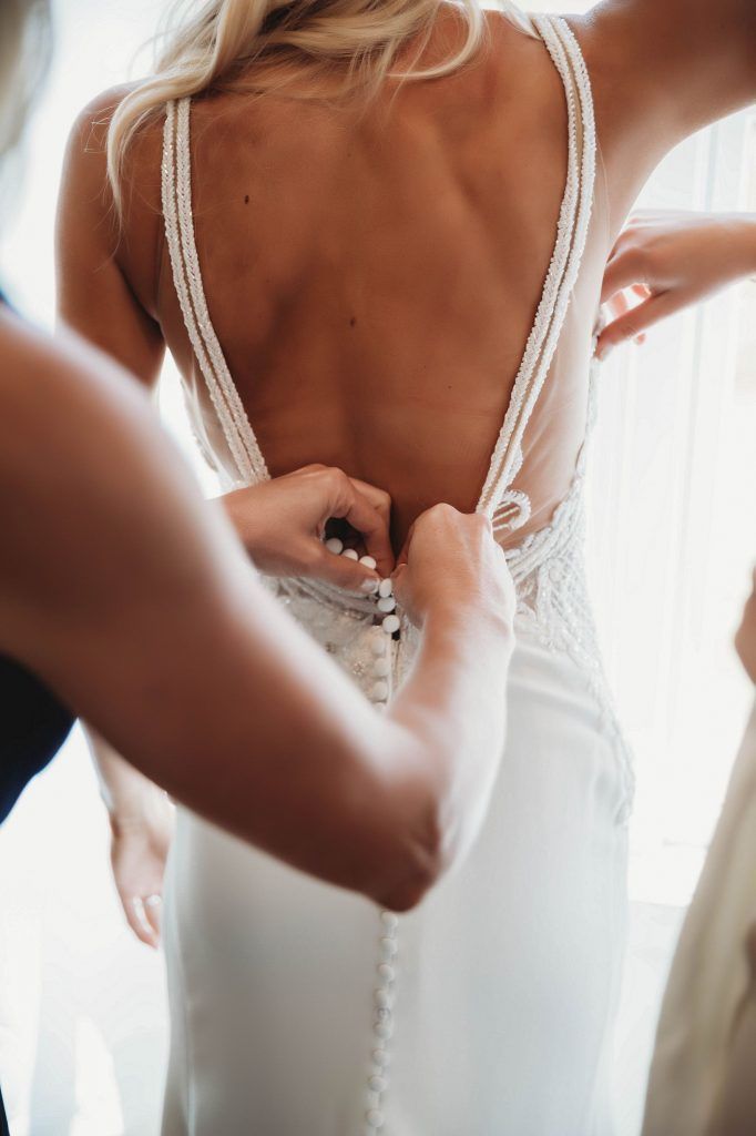 Woman's wedding dress being buttoned up, pearls on straps and back detail.