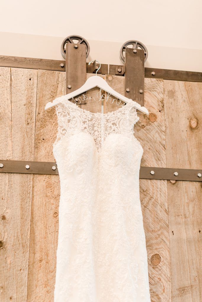 White lace wedding dress hanging on a wooden barn door.
