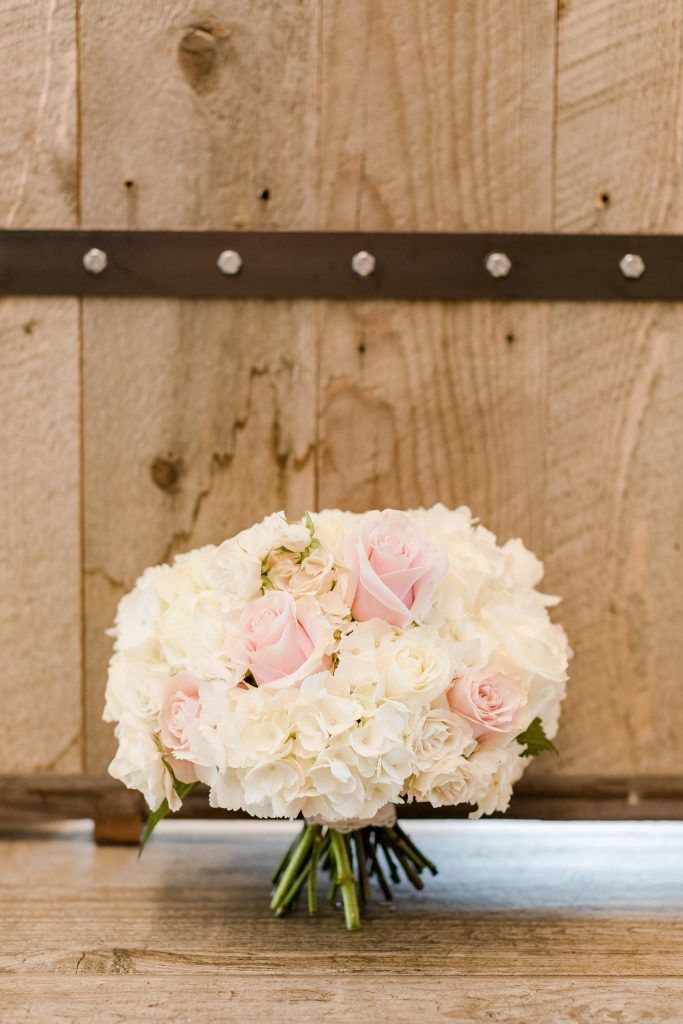 Bouquet of white hydrangeas and pink roses on wooden floor against a wooden door.