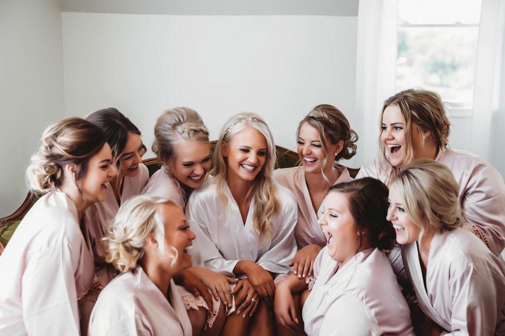 Bridesmaids in pink robes laugh together in a room.