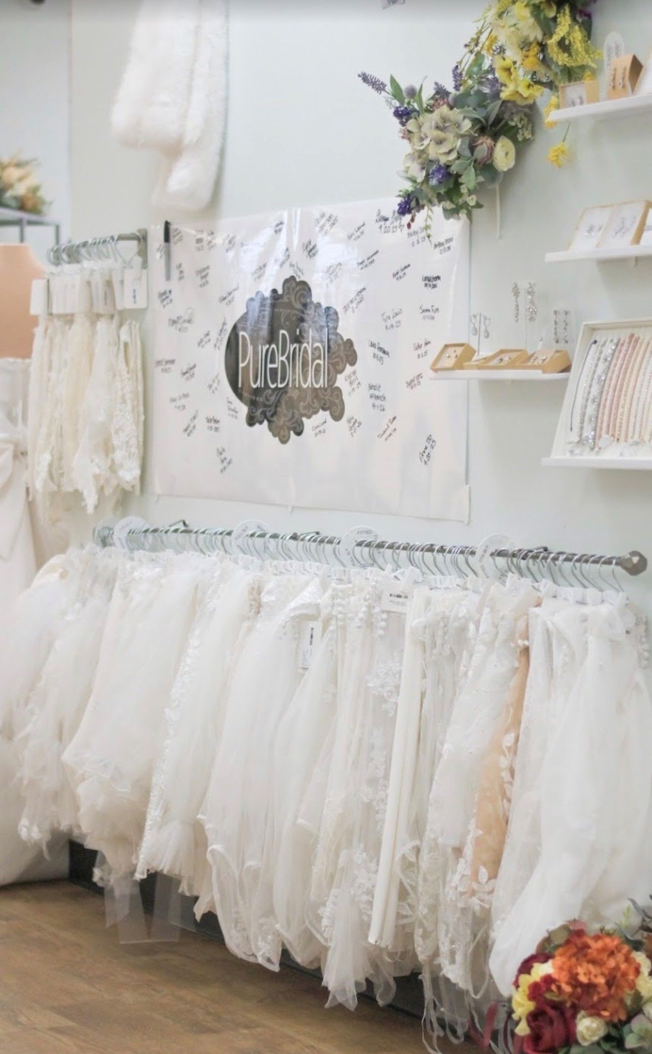 Bridal shop interior with dresses on racks, accessories on display, and wooden floors.