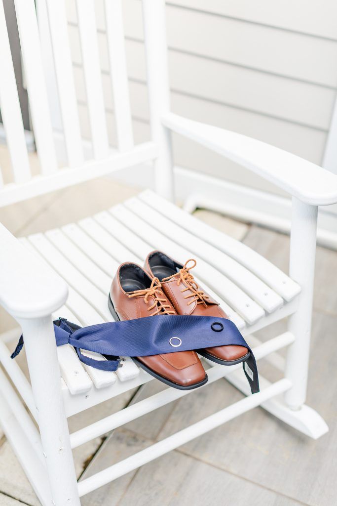 Brown dress shoes and navy tie on a white rocking chair with striped seat.