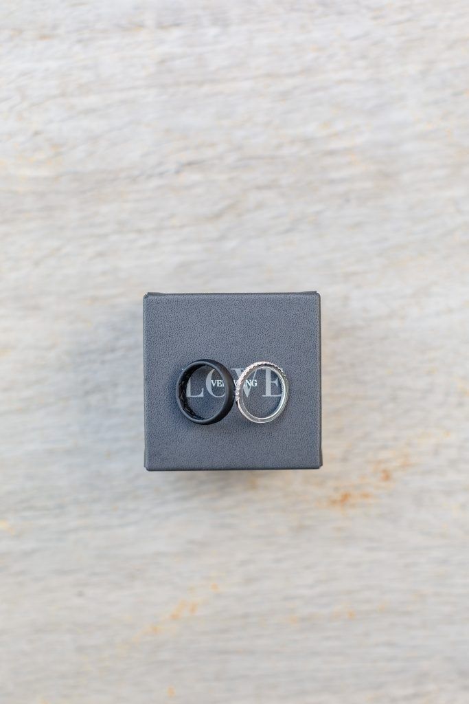 Two rings, one black, one silver, on a gray box. Light wood background.