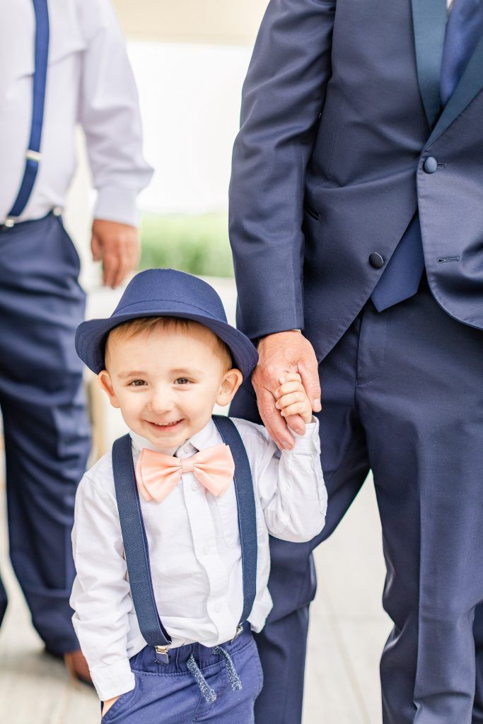 Boy in fedora, bow tie, suspenders holding hands with a man wearing a suit; both smiling.